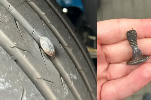 Przebita opona z wbitym gwoździem. W dłoni trzymam wyjęty z opony metalowy element, który spowodował uszkodzenie.