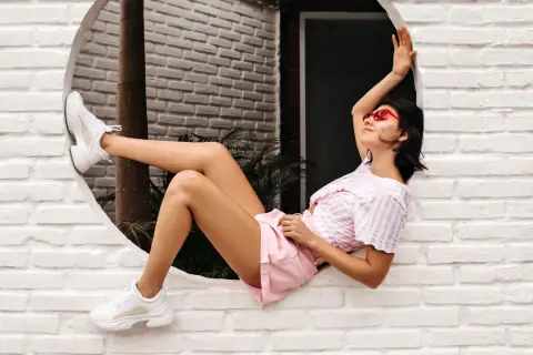 Ragazza con occhiali rossi e cljd scarpe bianche, sdraiata su un davanzale bianco.