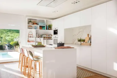 Elegante mueble cocina isla blanco con taburetes, encimera de cuarzo y vistas a un jardín con piscina.