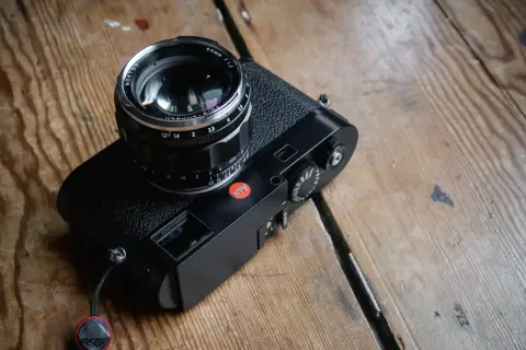 A black Leica M262 camera with a Nokton 50mm f/1.2 lens sits on a wooden surface.