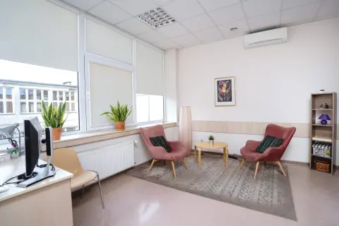 Jasne, przytulne wnętrze gabinetu psychologicznego z dwoma różowymi fotelami i stolikiem.
