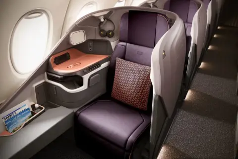 Luxuriöser Sitzbereich in der **besten Business Class** mit lila Ledersitzen, Kissen und einem Fenster.