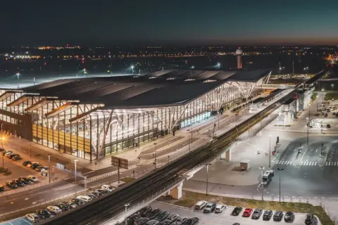 Nowoczesny terminal lotniska w Gdańsku nocą. Widok z góry pokazuje parkingi, drogi i tory kolejowe, ułatwiając planowanie, jak dojechać na lotnisko w Gdańsku.