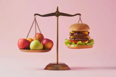 Waga pokazuje nierównowagę: owoce po jednej stronie, burger po drugiej. Zastanawiasz się nad zakwaszeniem organizmu objawy?