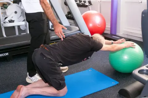Un homme fait des exercices pour soulager son arthrose lombaire, guidé par un kinésithérapeute.