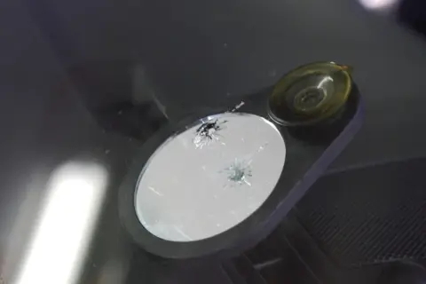 Uszkodzona szyba samochodowa z pęknięciami, czekająca na naprawę.