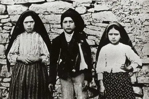Trójka dzieci, w tym siostra Łucja z Fatimy, pozuje przed kamiennym murem.