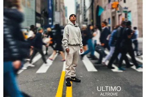 A young man in a grey tracksuit stands on a crosswalk in a busy city street, looking up.