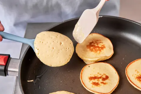 Pancakes rezept mit joghurt: goldbraune Pfannkuchen werden in einer Pfanne gebacken, ein Löffel Teig wird hinzugefügt.