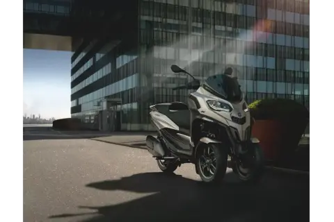 Nowoczesny Piaggio MP3, czy wersja 400 czy 500, parkuje przed szklanym budynkiem.
