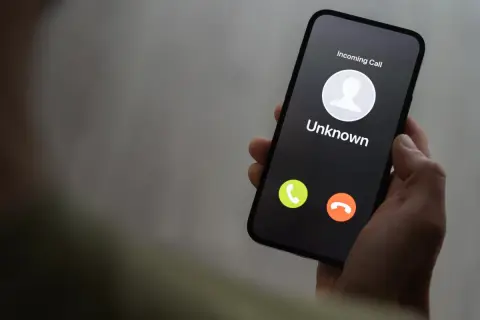 Dłoń trzyma smartfon z ekranem pokazującym przychodzące połączenie od nieznanego numeru. Czy to kolejny **wangiri**?