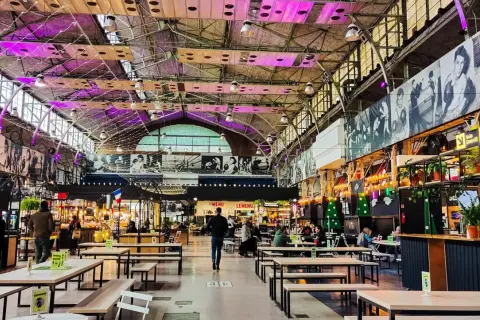 Wnętrze nowoczesnej vege restauracji w Warszawie. Widać stoły, ławki i stoiska z jedzeniem pod industrialnym dachem.