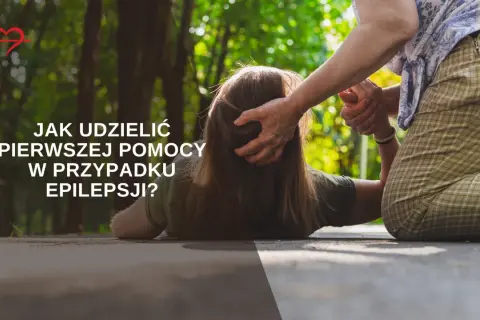 Starsza osoba pomaga osobie leżącej na ziemi, udzielając pierwszej pomocy w przypadku **epilepsji**.