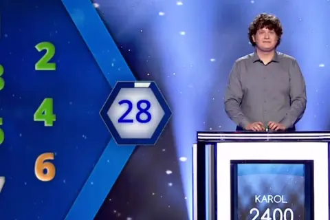 Karol Fedoruk w studiu telewizyjnym, obok planszy z liczbami i wynikiem 2400.
