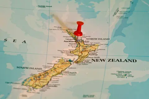 Czerwony pinezka zaznacza Nową Zelandię na mapie. To państwo wyspiarskie, które geograficznie należy do Oceanii, choć kulturowo i politycznie często kojarzone jest z Australią, która leży na kontynencie australijskim.