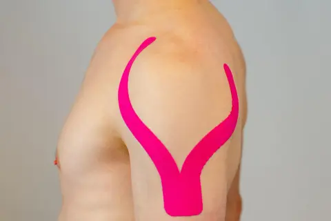 Schulter tapen: Ein Mann mit pinkem Kinesio-Tape auf der Schulter, das wie ein aufgeschlagenes Buch aussieht.