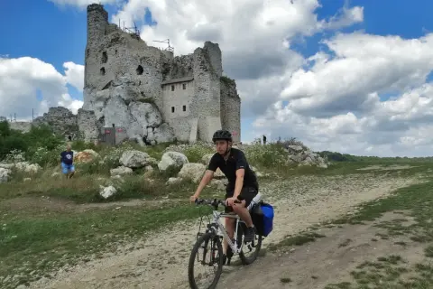 Młody mężczyzna na rowerze przemierza malowniczą trasę po Jurze Krakowsko-Częstochowskiej, mijając ruiny zamku.