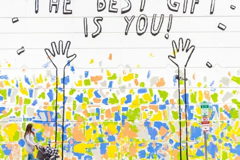 Bunte Wandmalerei mit der Botschaft "The best gift is you!". Eine Frau schiebt einen Kinderwagen. Dies erinnert an die psychologischen werte tests, die uns lehren, uns selbst wertzuschätzen.