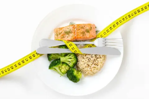 Gesundes Essen für schnelles Abnehmen: Lachs, Brokkoli und Reis, umgeben von einem Maßband.