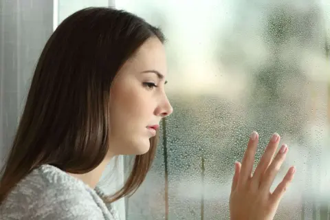Smutna dziewczyna patrzy przez zaparowane okno. Jej dłoń dotyka szyby, jakby szukając wyjścia z tej potocznie zwanej depresji psychicznej.