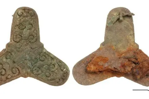 Zwei bronzene Artefakte, ein gut erhaltenes mit Verzierungen, das andere stark verrostet, stammen aus einem Wikinger Grab.