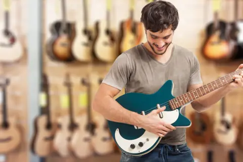 Młody mężczyzna wybiera **jaką gitarę elektryczną na początek** w sklepie muzycznym.
