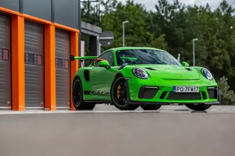 Jaskrawozielony Porsche 911 GT3 RS z czarnym spojlerem i felgami, gotowy do wyjazdu z garażu.