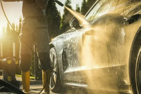 Słońce zachodzi, a Ty uczysz się, jak myć auto na myjni ciśnieniowej. Woda spływa po lśniącej karoserii.