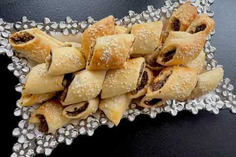 Paszteciki z pieczarkami i serem, posypane sezamem, ułożone na ozdobnej tacy z kwiatowymi zdobieniami.