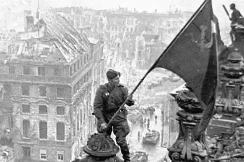Soldat hisst Flagge über zerstörter Stadt. Berlin, 8. Mai Feiertag.