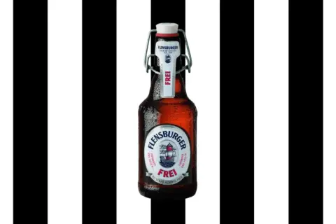 Flasche Flensburger Pilsener Alkoholfrei, mit Bügelverschluss, vor schwarz-weißen Streifen.