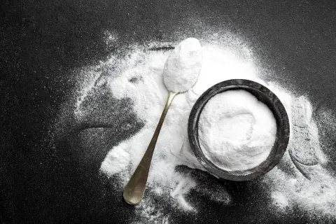 Un cucchiaio e una ciotola pieni di carbonato di sodio, mostrando i suoi molteplici usi in cucina e per la pulizia.