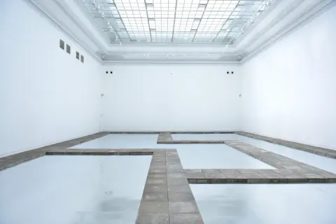 Biała przestrzeń galerii z lustrzaną podłogą i kamiennymi ścieżkami tworzącymi labirynt. Kojący widok, jakbyś spacerował po chmurach.