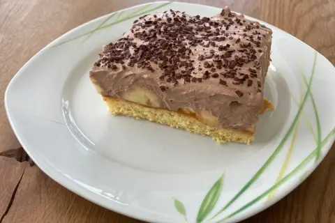 Ein Stück Bananen Torte mit Schokoladencreme und Schokostreuseln auf einem Teller mit Blattmuster.