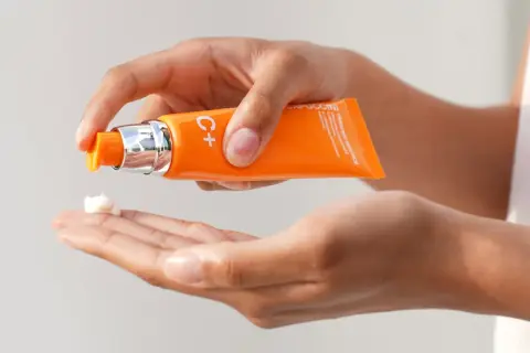 Mani che dosano una crema con vitamina C sulla pelle, per un trattamento illuminante e antiossidante.