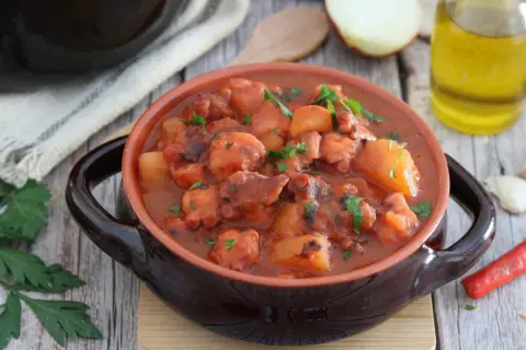 Un saporito polpo alla pignata, con patate e prezzemolo, servito in una ciotola di terracotta.