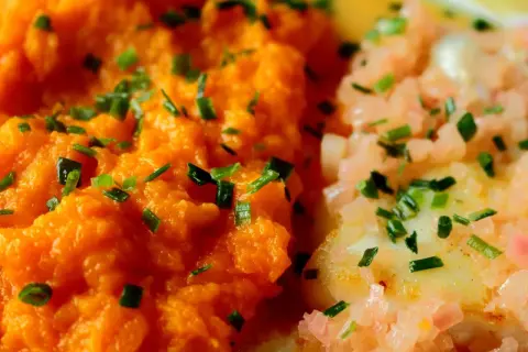 Purée de carotte onctueuse, parsemée de ciboulette fraîche, à côté d'un plat de poisson aux oignons roses. Un délice coloré.