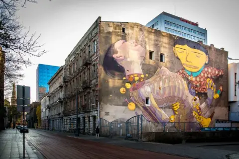 Imponujące street art na ścianie kamienicy, przedstawiające surrealistyczną scenę z postaciami i elementami anatomicznymi.