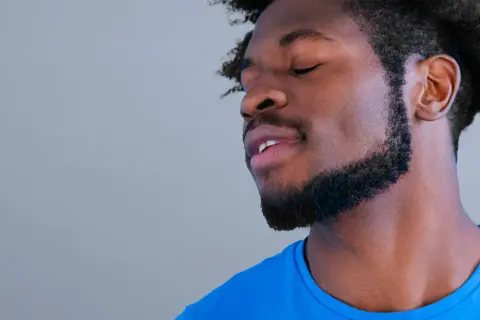 Un homme avec une barbe collier épaisse, les yeux fermés, porte un t-shirt bleu vif.