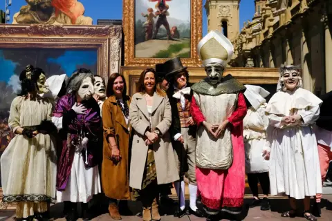 Personas enmascaradas y vestidas con trajes de época posan frente a cuadros, recreando el espíritu de las fiestas goyescas.