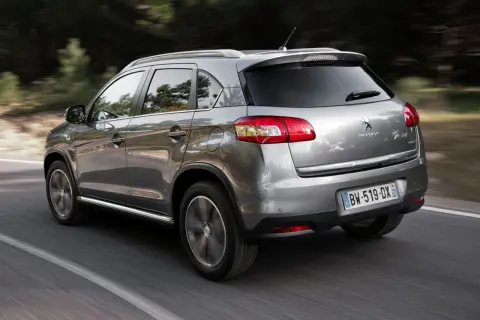 Srebrny Peugeot 4008 jedzie po drodze wśród drzew.