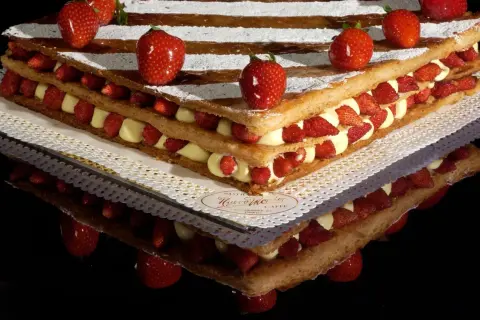 Una magnifica torta millefoglie con strati di pasta sfoglia, crema pasticcera e fragole fresche, decorata con fragole intere e zucchero a velo.