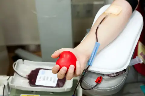 Dłoń trzymająca czerwone serce podczas oddawania krwi. Zastanawiasz się, ile dni wolnego za oddanie krwi? To ważna decyzja.