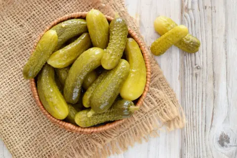 Koszyk pełen kiszonych ogórków na jutowym płótnie. Zastanawiasz się, ile kcal ma ogórek kiszony? To zdrowa przekąska!