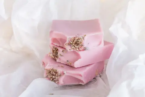 Zarte rosa Seifenstücke mit Lavendelblüten, inspiriert von Quillaja Saponaria, liegen auf weißem Papier.