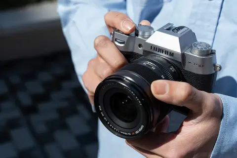 Dłonie trzymające srebrny aparat Fujifilm X-T50 z obiektywem Fujinon.