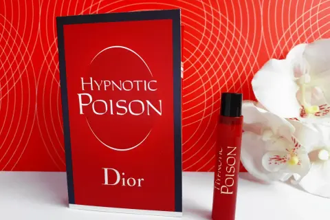 Kuszący zapach Christian Dior Hypnotic Poison w czerwonym flakonie obok karty z nazwą.