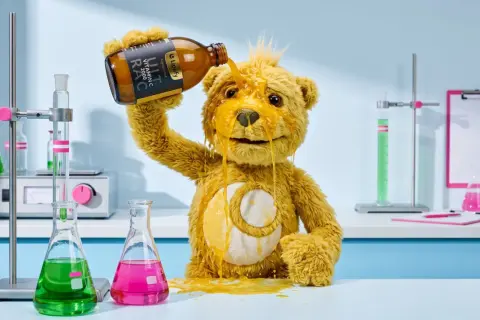 Ein Teddybär kippt eine Flasche Vitamin C über sich. Sieht aus, als hätte er zu viel Vitamin C genommen und nun klebt alles.