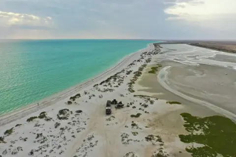 Pustynna plaża z turkusową wodą, gdzie jest Oman. Obóz z samochodami terenowymi i namiotem na piasku.