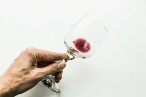 Mano che tiene un bicchiere di vino rosso, con un residuo che ricorda l'acido tartarico, essenziale per la sua conservazione.